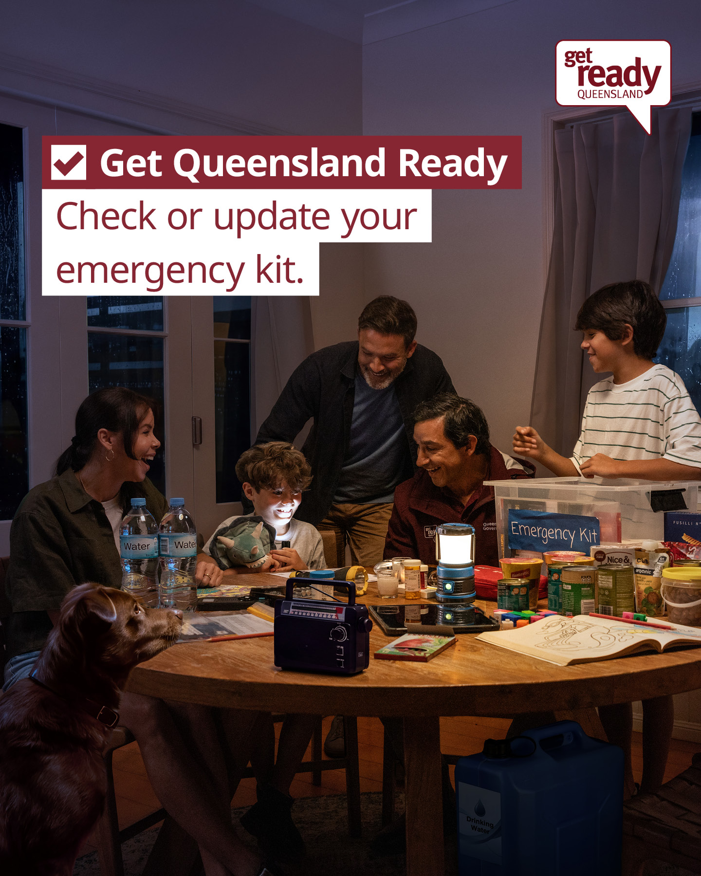 A family sit around a table with an emergency kit containing food, a battery radio and a first aid kit