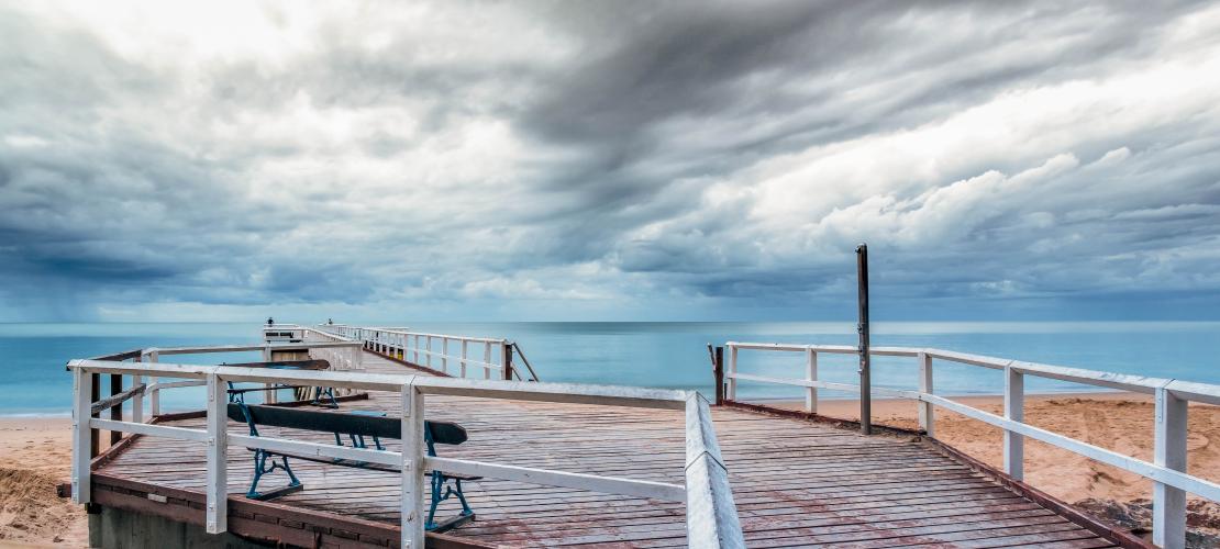 Pier on beach with stormy sky