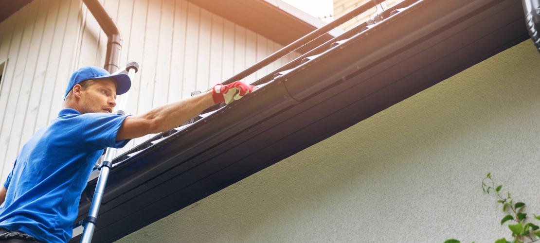 Man on ladder cleaning gutters