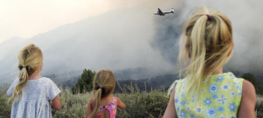 Kids looking at plane and fire in distance
