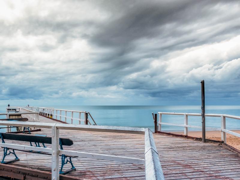 Pier on beach with stormy sky