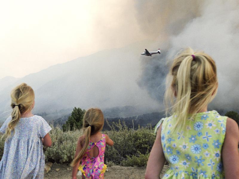 Three children watching bushfires be extinguished by a water bomber plane.